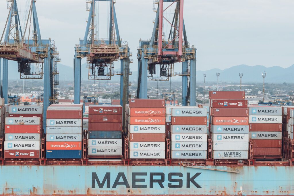 Large cargo ship loaded with shipping containers at a busy industrial port.