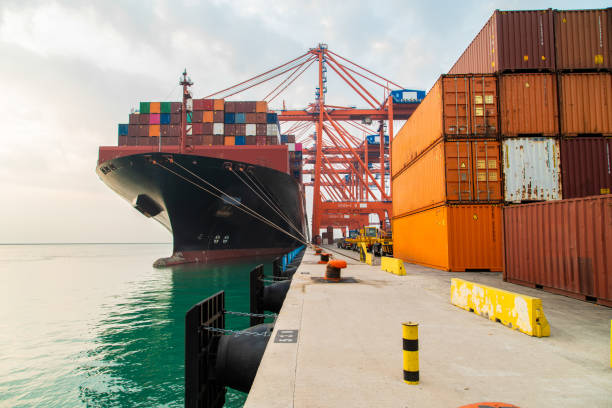 Cargo container ship moored at harbor. Loading or unloading containers with cranes.